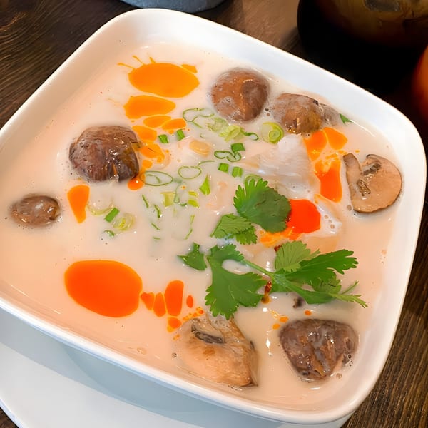 Creamy Thai soup with mushrooms, green onions, cilantro, and chili oil in a white bowl.