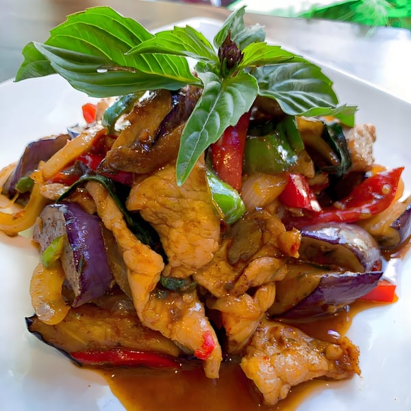 One More Thai's spicy stir-fried chicken with eggplant, bell peppers, and basil on a white plate.