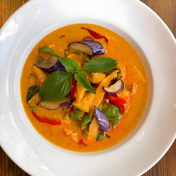 One More Thai red curry with chicken, eggplant, bell peppers, and basil in a white bowl.