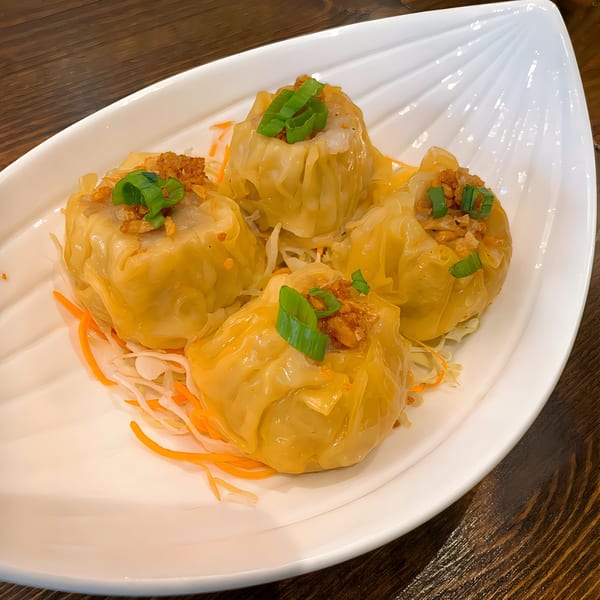Four Thai dumplings, garnished with green onions and fried garlic, on a white leaf-shaped plate.