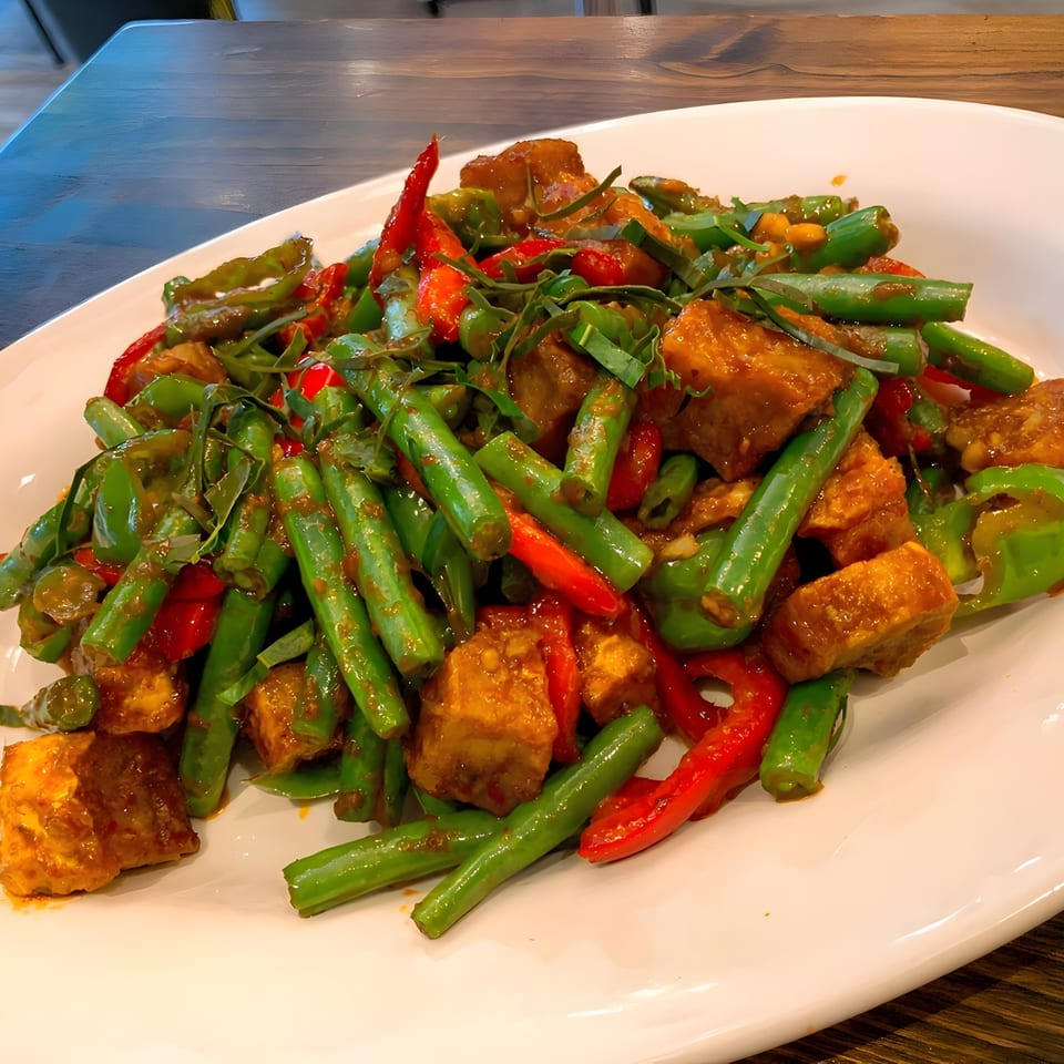 One More Thai's Pad Prik Khing with crispy tofu, green beans, and red chili on a white plate.